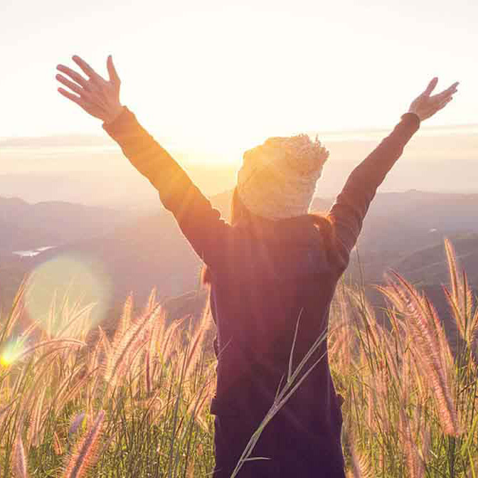 vrouw met armen in de lucht in de zon in een akker met bergen op achtergrond