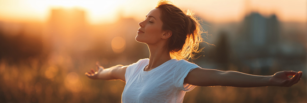 A woman with her arms outstretched, enjoying the fresh air and sunshine on a summer day, in a panoramic banner. 