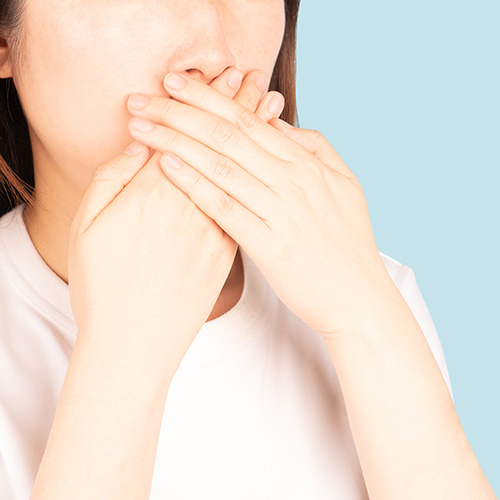 Close up of asian woman covering her mouth with her hands isolated on blue background.